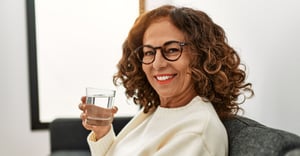 Senior woman smiling and drinking a glass of water on the couch