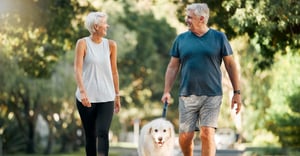 Two senior adults walking their dog outside